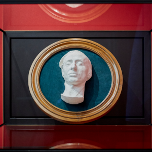 Eksponowana w Muzeum Książąt Czartoryskich jasna rzeźba przedstawiająca głowę mężczyzny ułożona na niebieskiej tkaninie otoczonej drewnianą owalną ramą.
